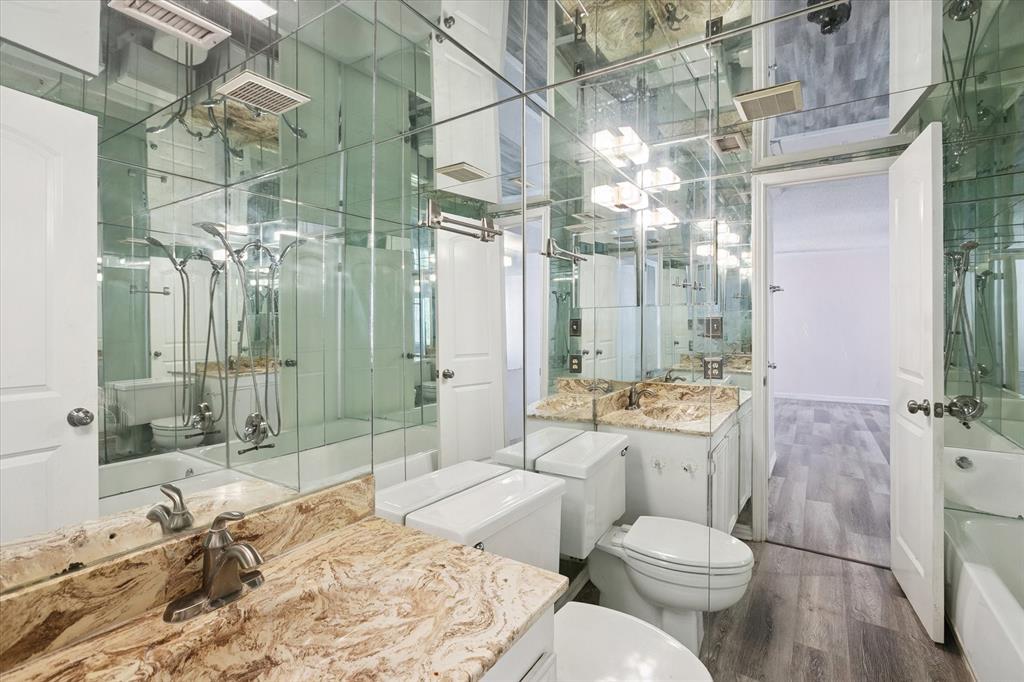 Bathroom featuring floor-to-ceiling mirrored walls, vanity with stone-finish countertop, undermount sink, multi-light fixture, and wood-finish flooring