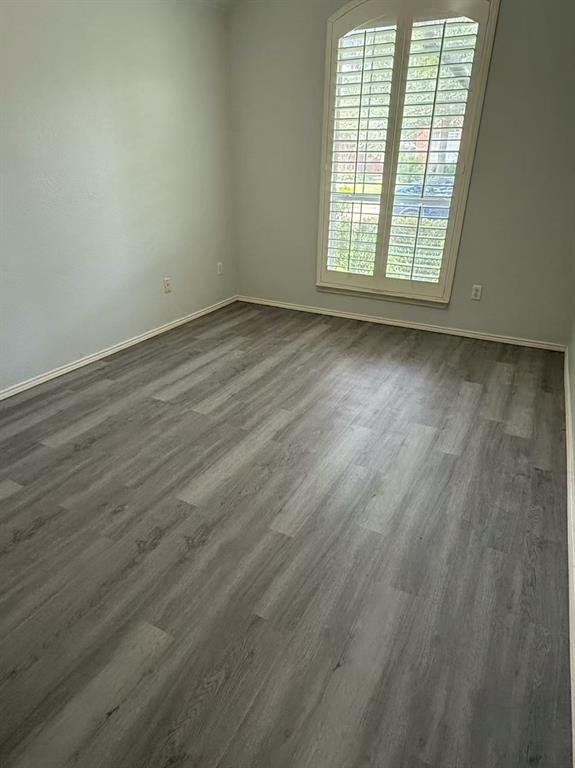 Neutral-toned interior space featuring wood-finish flooring, an arched window, and custom interior shutters