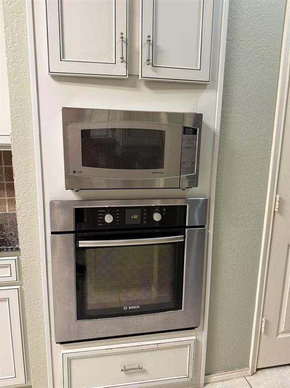 Built-in stainless steel oven and microwave, white shaker-style cabinetry with satin nickel hardware, and lower storage drawer