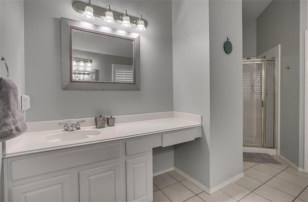 Bathroom featuring a white vanity with an integrated countertop, four-light vanity fixture, framed wall mirror, and a glass-enclosed shower stall with tile flooring