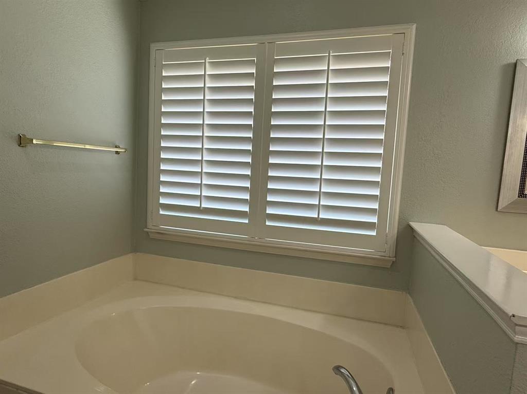 Soaking tub featuring a white surround and polished chrome faucet, paired with white plantation shutters and a wall-mounted metal towel bar