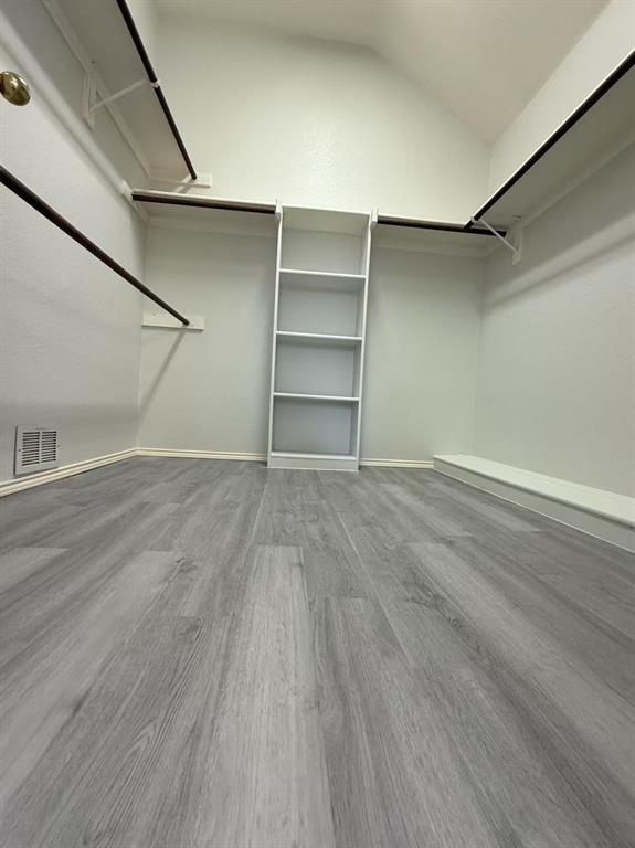 Walk-in closet featuring wood-finish flooring, built-in shelving, and dual-level hanging rods