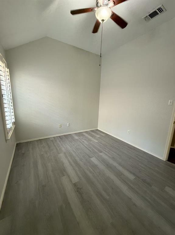 Vaulted ceiling featuring a central wooden-blade ceiling fan, shutter-style window coverings, and neutral wood-finish flooring