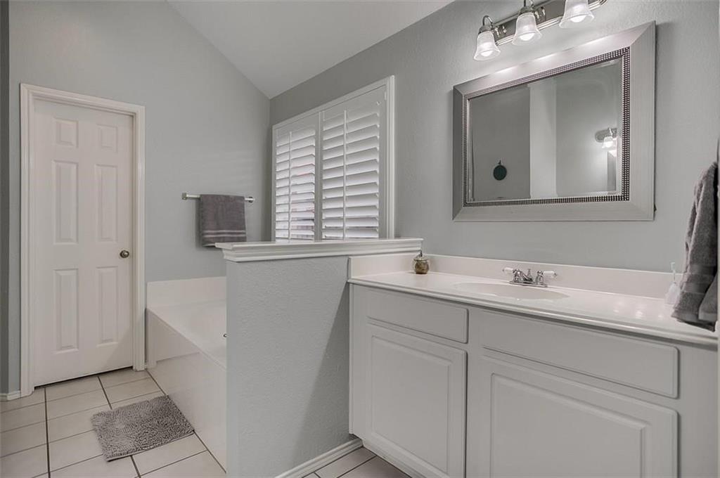 White vanity featuring an integrated sink, vaulted ceiling, white plantation shutters, and a three-light vanity fixture
