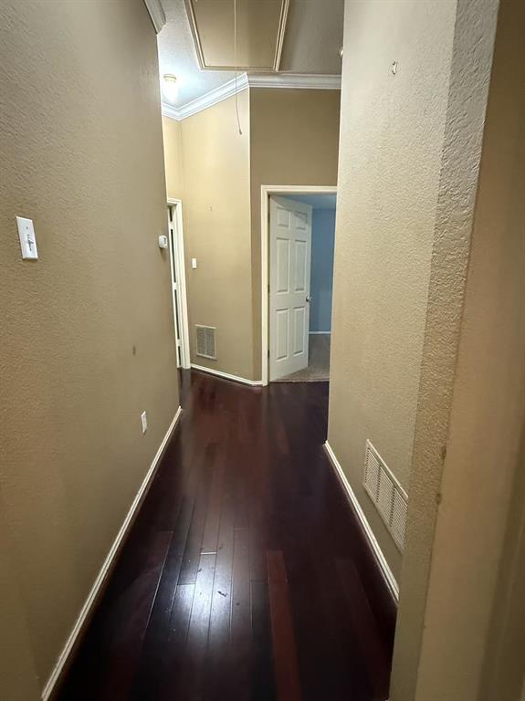 Hallway featuring dark wood-finish flooring, neutral wall paint, crown molding, and two-panel interior doors