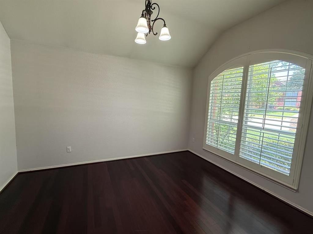 Room featuring vaulted ceilings, wood-finish flooring, an arched window with plantation shutters, and a three-light chandelier