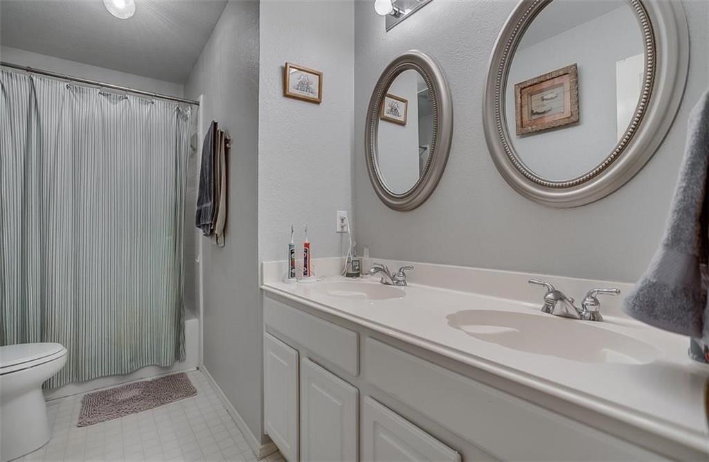 Dual-sink vanity with a solid-surface countertop, two oval wall-mounted mirrors, chrome plumbing fixtures, and a shower-tub combination with an enclosure