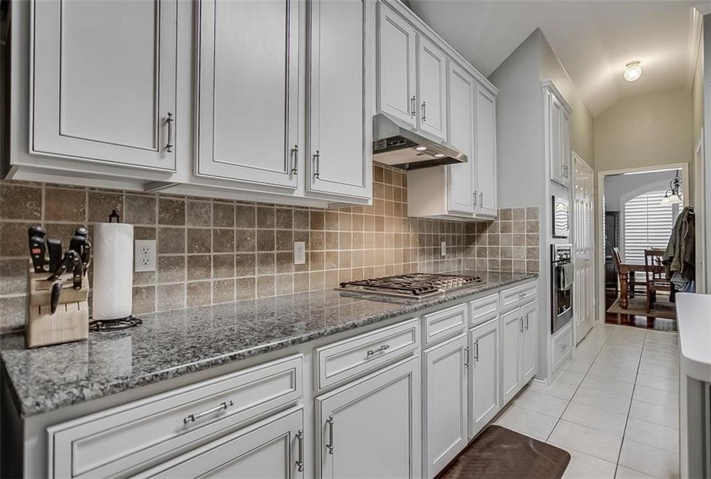 Kitchen featuring crisp white shaker-style cabinetry, polished stone countertops, a neutral tiled backsplash, a built-in stainless steel gas cooktop, and a recessed wall oven