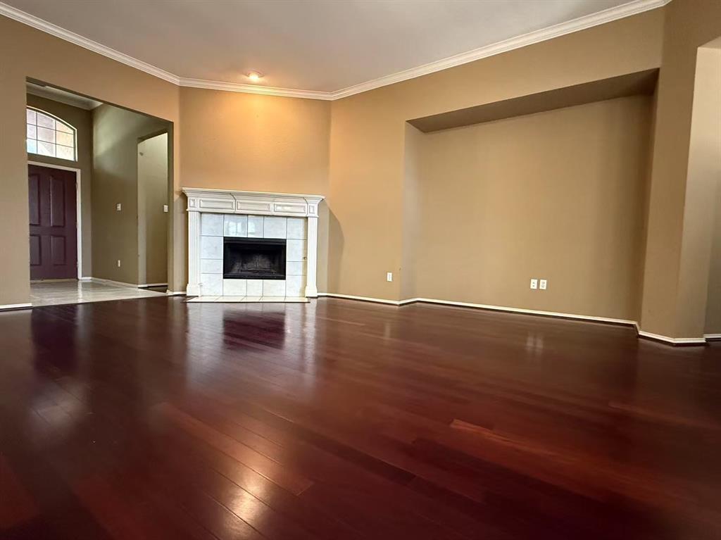 Living area featuring wood-finish flooring, a corner fireplace with a decorative mantel, crown molding, and a recessed wall niche