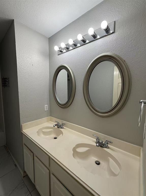 Dual-basin vanity featuring an integrated countertop, two oval wall-mounted mirrors with metallic frames, and a six-bulb vanity light fixture