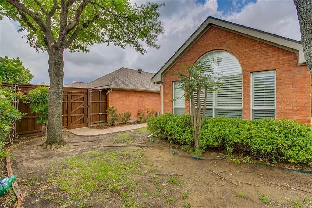 Exterior red brick facade featuring a large arched window with horizontal blinds, a concrete side path, and a wooden privacy fence