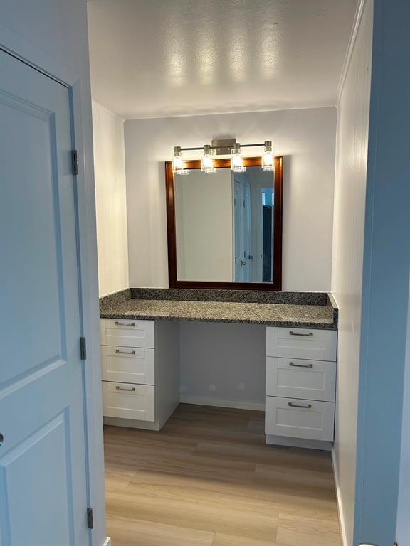 Built-in vanity featuring white cabinetry, stone-finish countertop, wood-finish flooring, a wall-mounted mirror with a dark wood frame, and a four-light fixture