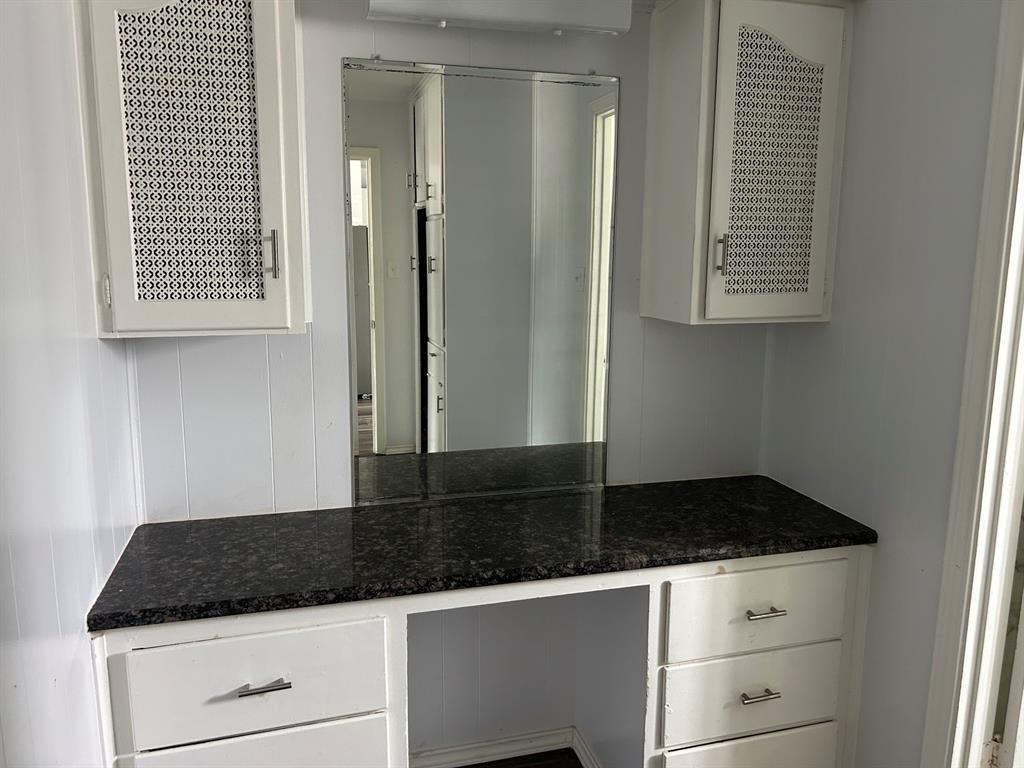 Built-in vanity featuring white cabinetry, dark stone-finish countertop, upper wall-mounted storage cabinets with decorative mesh panels, and a full-height mirror