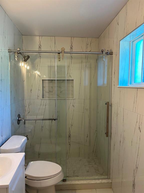 Shower enclosure featuring floor-to-ceiling large-format tile with veining, a glass sliding door with stainless steel hardware, an integrated recessed wall niche, and a stainless steel shower head