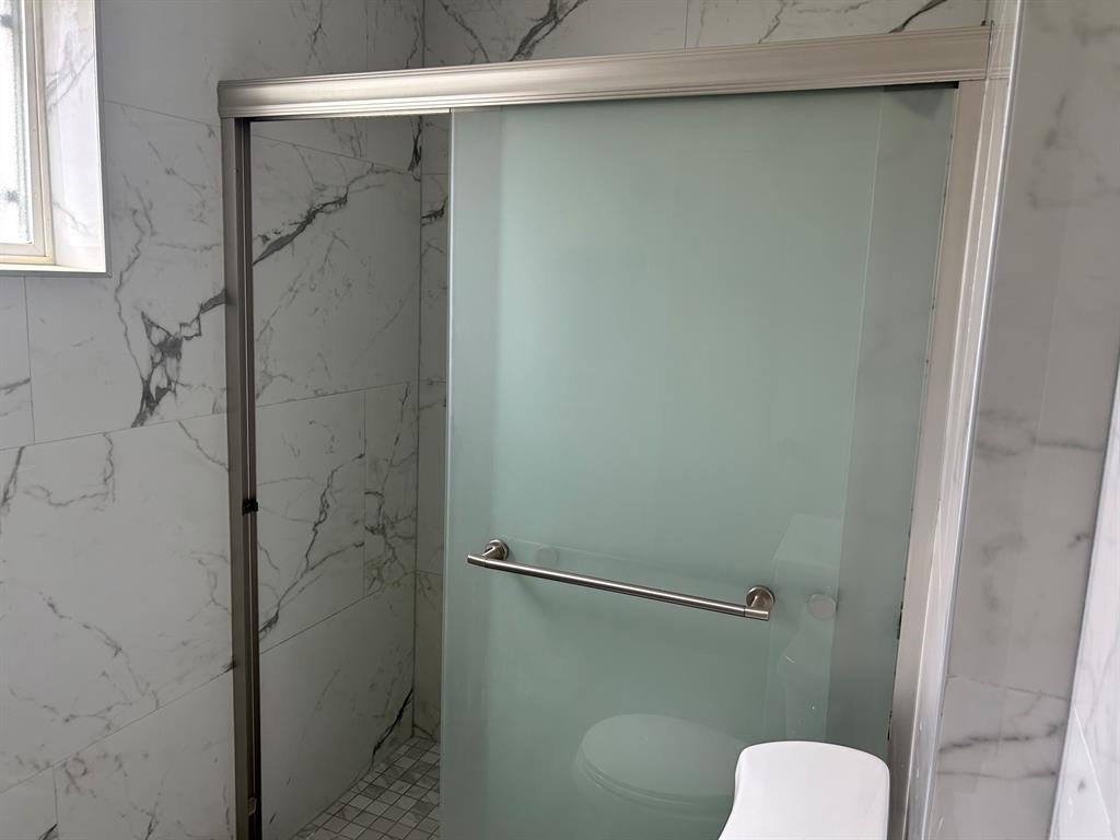 Shower stall featuring large-format wall tile with veining, frosted glass sliding door, brushed metal hardware, and mosaic floor tile