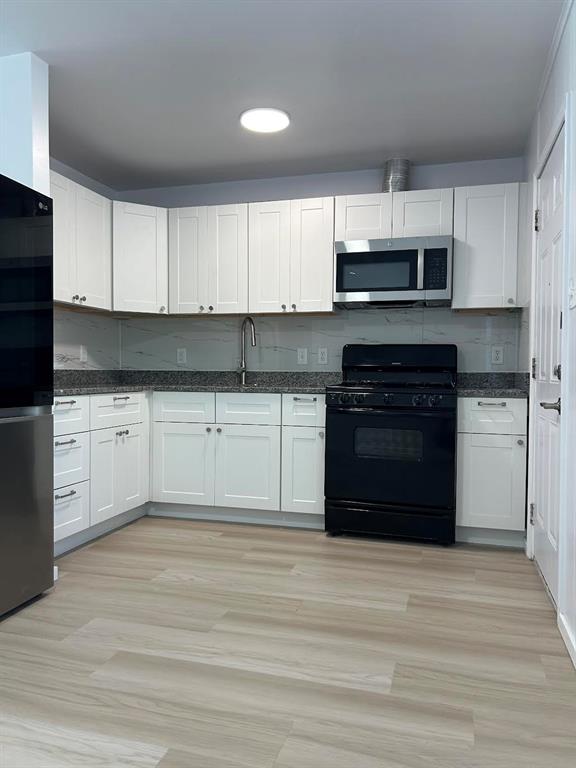 Kitchen featuring white shaker-style cabinetry, stone-finish countertops, light wood-finish flooring, and a stainless steel over-the-range microwave