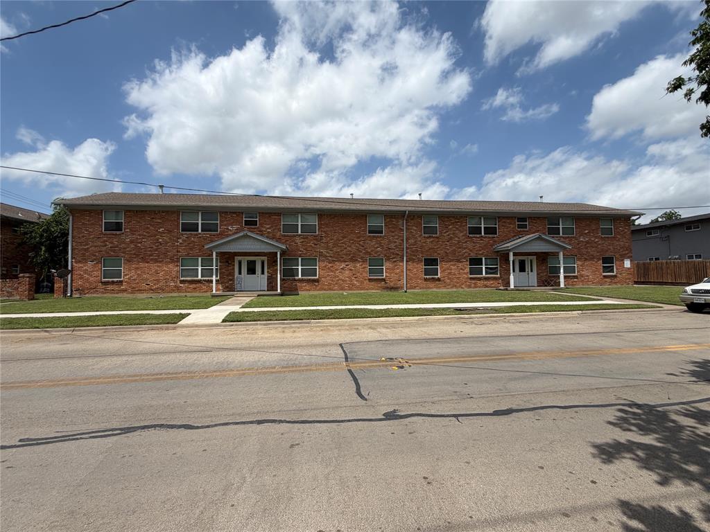 Multi-story brick exterior featuring dual covered entryways, a shingle roof, and a front lawn