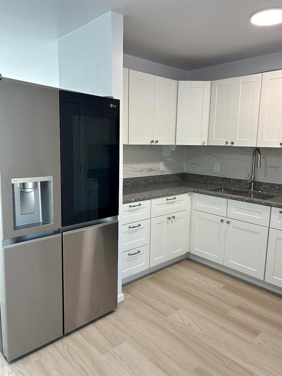 Kitchen featuring white shaker-style cabinetry, stone-finish countertops, stainless steel refrigerator, undermount sink with high-arc faucet, and light-tone wood-finish flooring