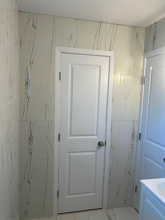 Full-height stone-patterned wall tile, white six-panel interior doors, and matching stone-patterned floor tile