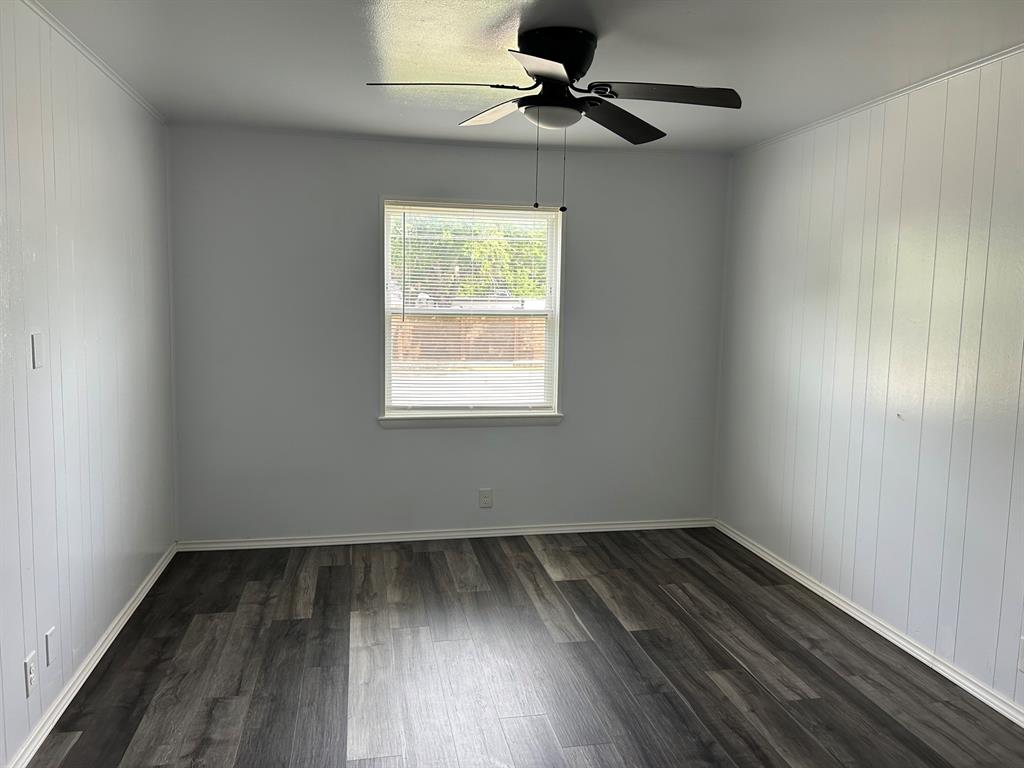 Room featuring wood-finish flooring, vertical paneling, and a ceiling fan with integrated lighting