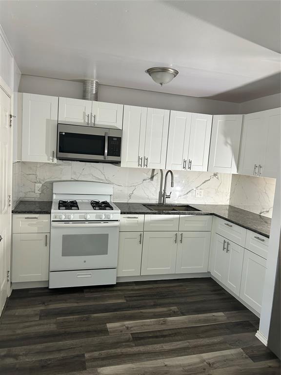 Kitchen featuring white Shaker-style cabinetry, dark stone-finish countertops, full-height decorative tile backsplash, wood-finish flooring, and a stainless steel over-the-range microwave
