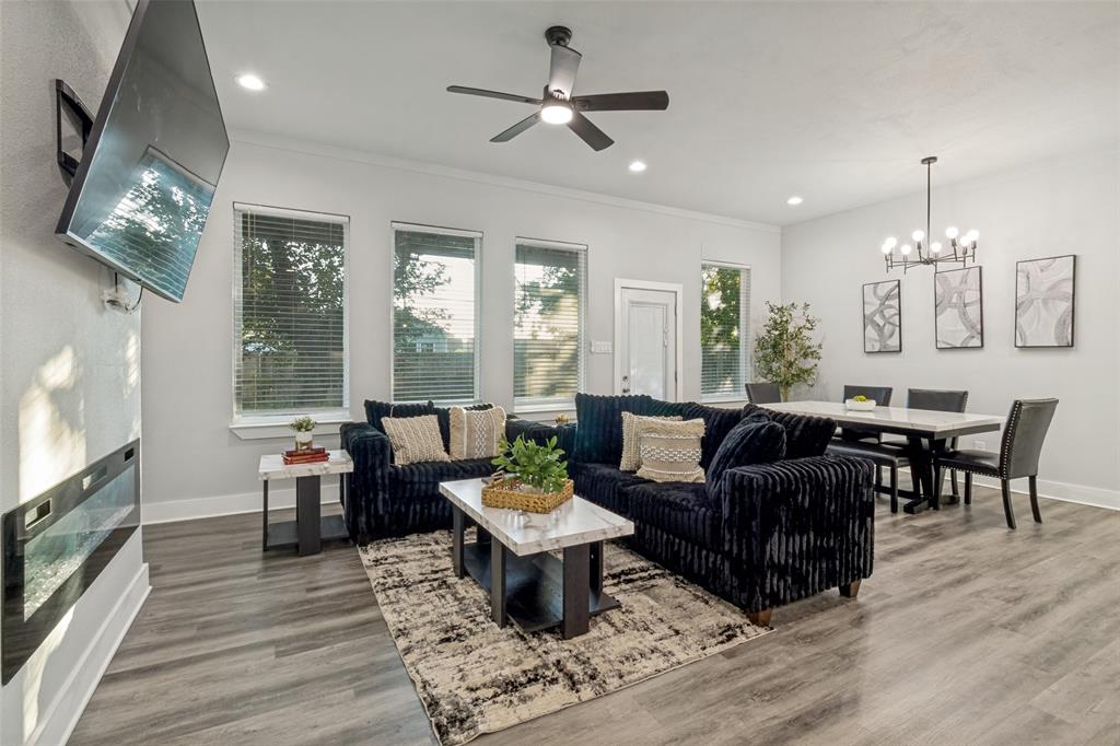 Open concept area featuring wood-finish flooring, recessed lighting, a modern wall-mounted electric fireplace, a multi-blade ceiling fan, and a multi-arm chandelier