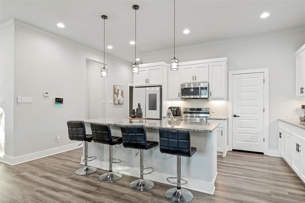 Kitchen featuring white cabinetry, stone countertops, stainless steel appliances, wood-finish flooring, and three pendant lights suspended over a breakfast bar