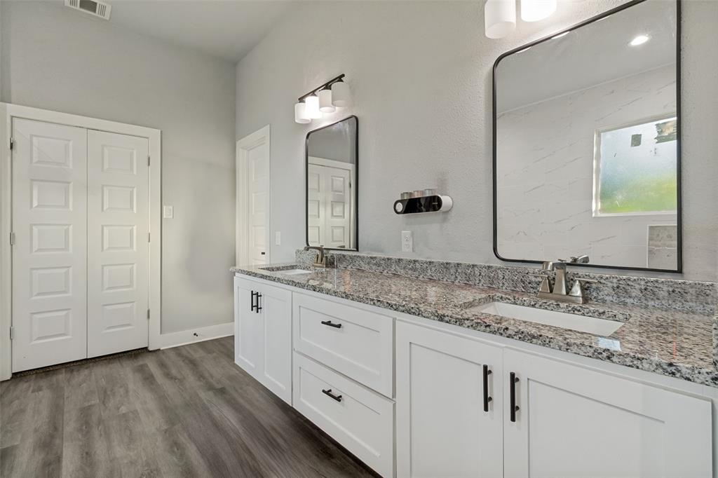 Dual-vanity bathroom featuring white cabinetry with matte black hardware, speckled stone-patterned countertops, dual rectangular under-mount sinks, wood-finish flooring, and framed mirrors