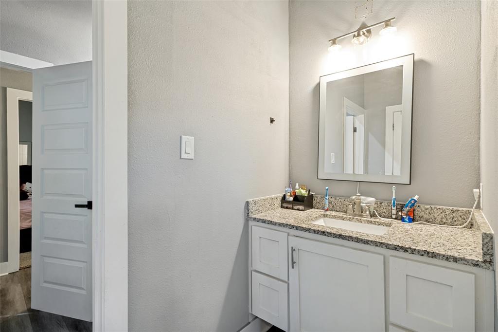 White shaker-style vanity featuring a stone-finish countertop, integrated rectangular sink, framed wall mirror, and three-bulb vanity light fixture