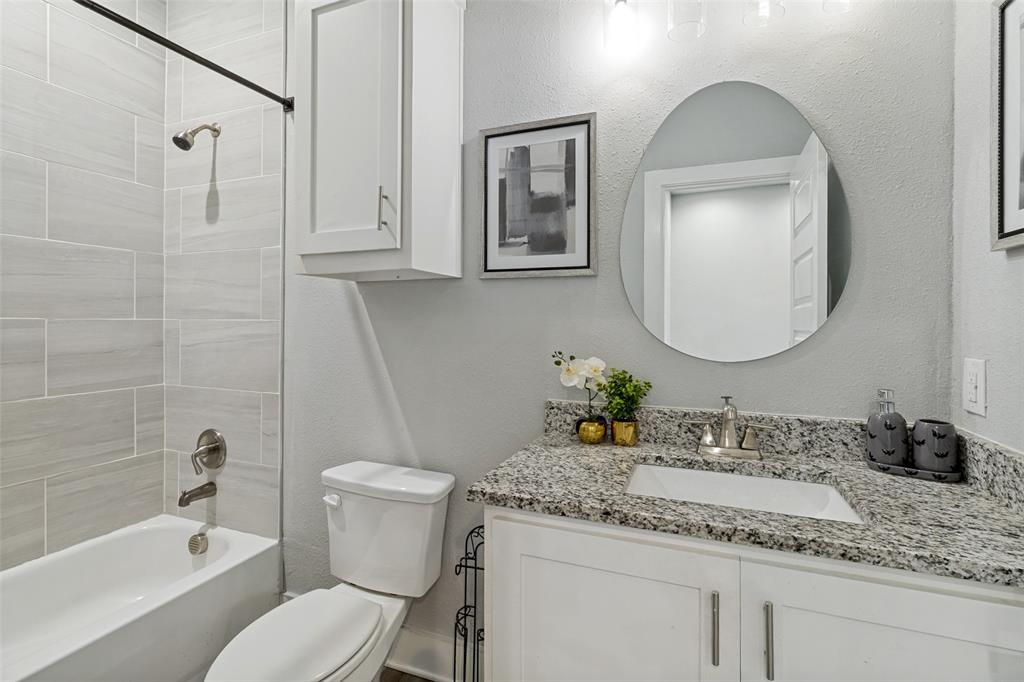 Bathroom featuring a stone-composite countertop, undermount sink, white cabinetry with brushed-nickel hardware, an oval wall-mounted mirror, and tile shower surround