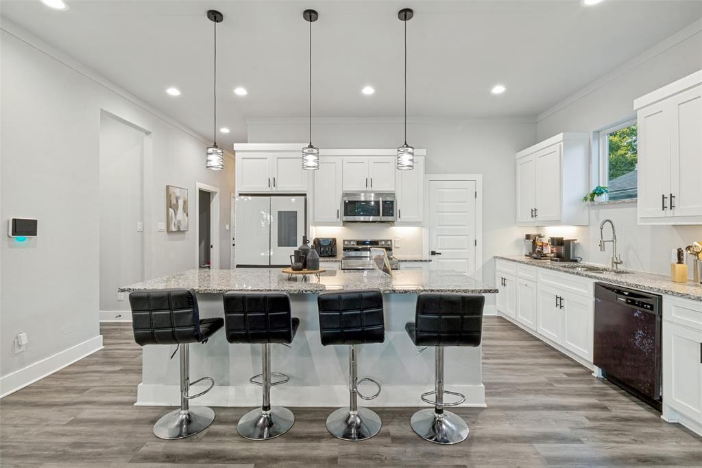 Kitchen featuring white cabinetry, stone countertops, stainless steel appliances, a center island with bar seating, and wood-finish flooring