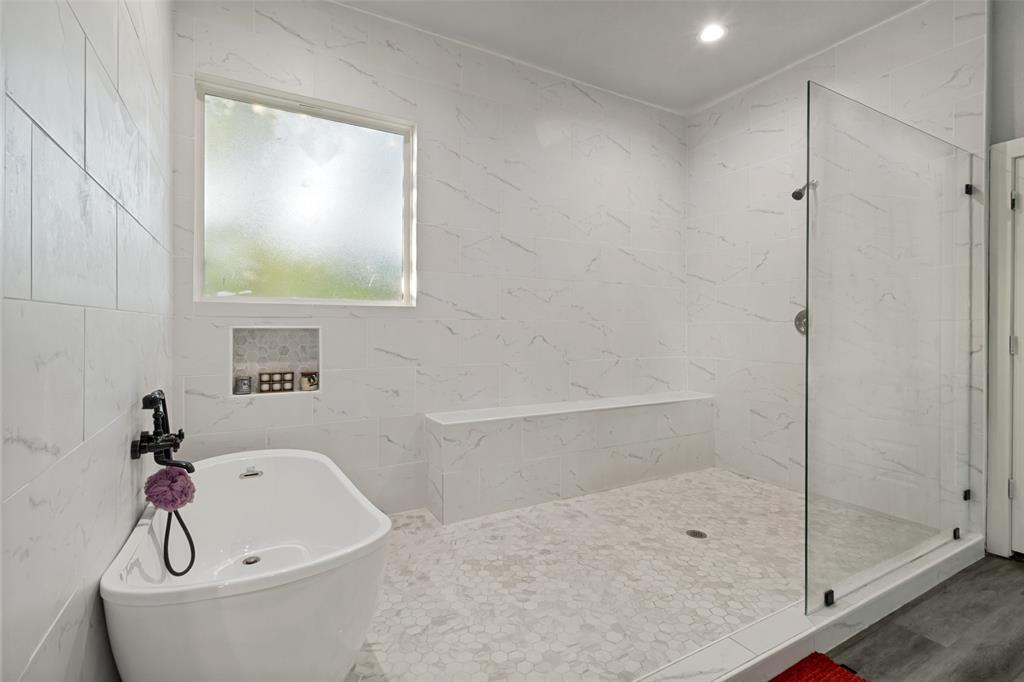 Freestanding soaking tub with a wall-mounted faucet, walk-in shower featuring a built-in bench, glass enclosure, and floor-to-ceiling stone-patterned wall tile