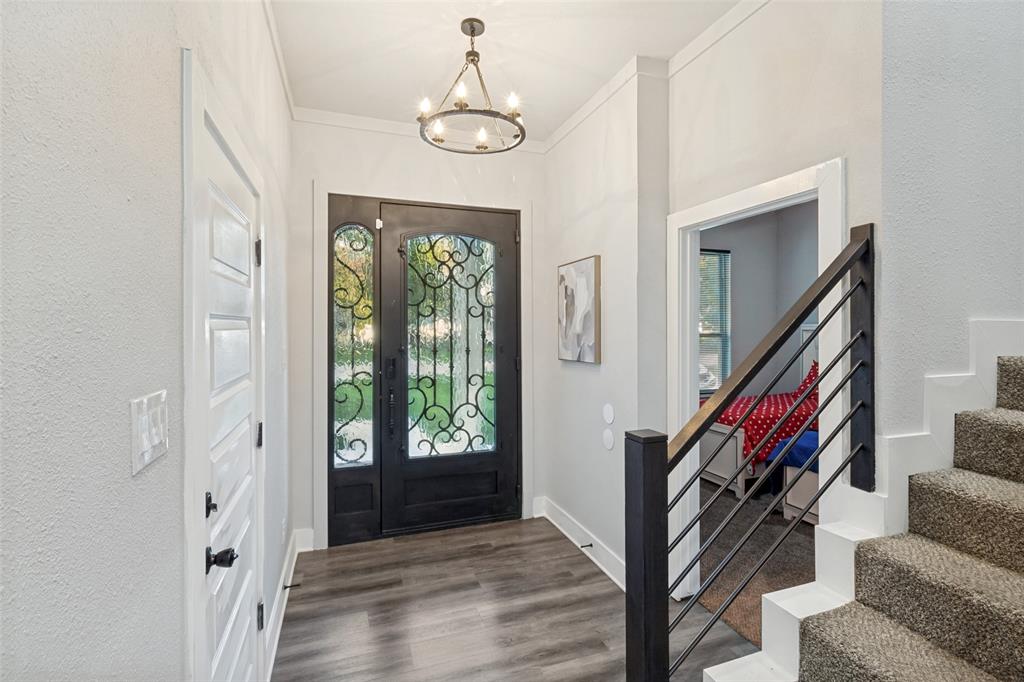 Entryway featuring a dark-finish iron-accented front door, wood-finish flooring, a tiered metal chandelier, and a staircase with a horizontal rail system