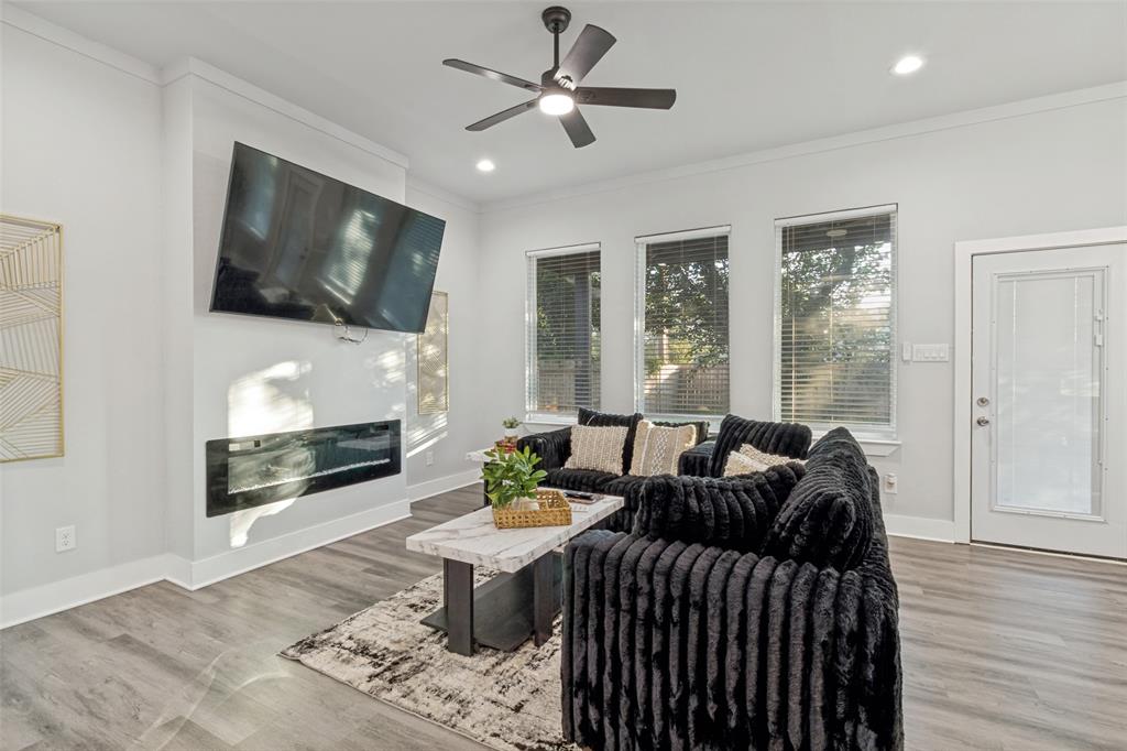 Living area featuring wood-finish flooring, a contemporary recessed linear fireplace, three windows with blinds, a modern ceiling fan, and a glass-paneled exterior door