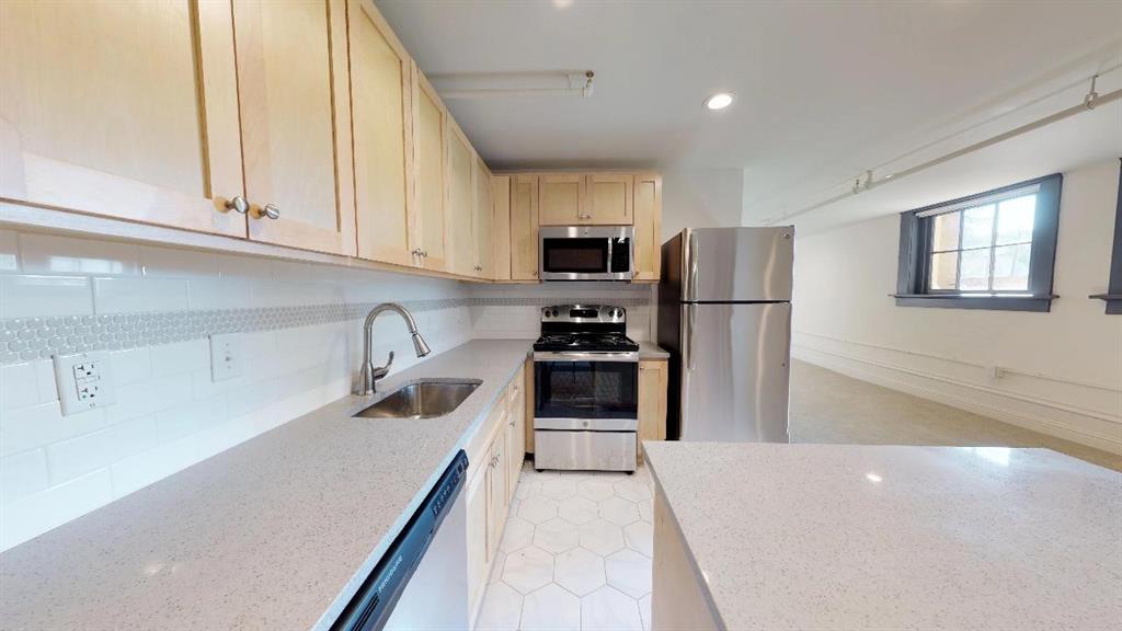 Kitchen featuring light brown cabinets, tasteful backsplash, light stone countertops, appliances with stainless steel finishes, and sink