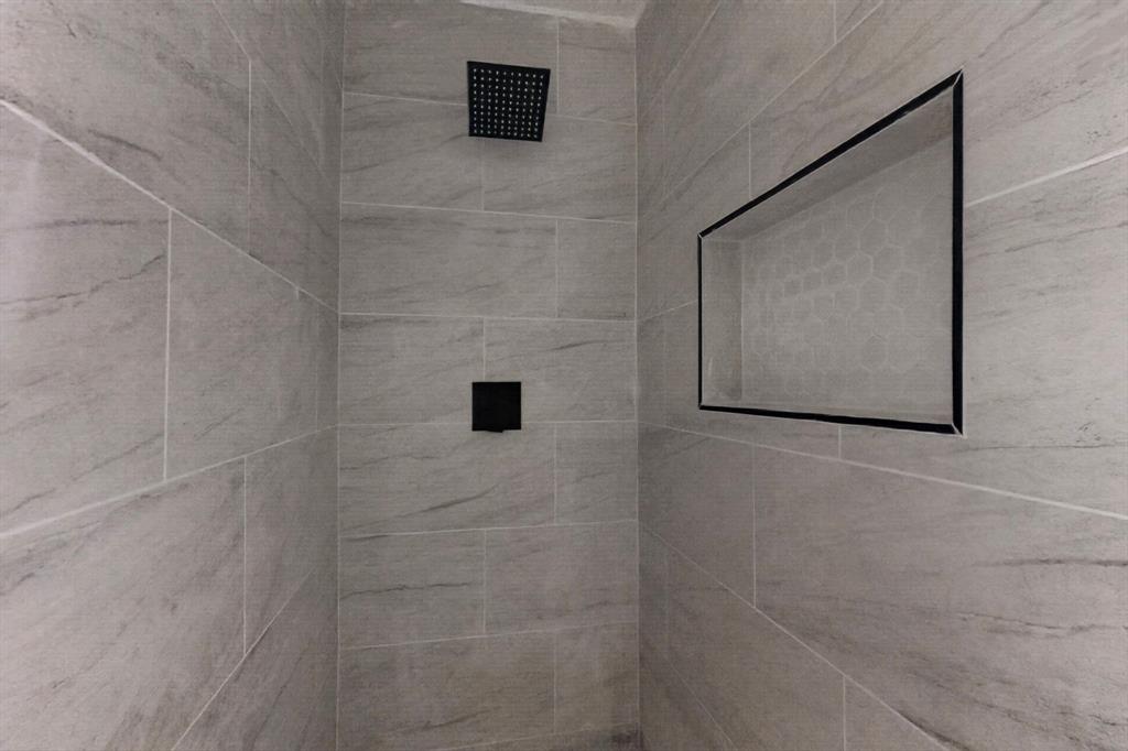 Walk-in shower featuring large-format light grey stone-patterned tile, matte black rain-style shower head, matte black single-handle mixing valve, and a recessed wall niche with a contrasting border