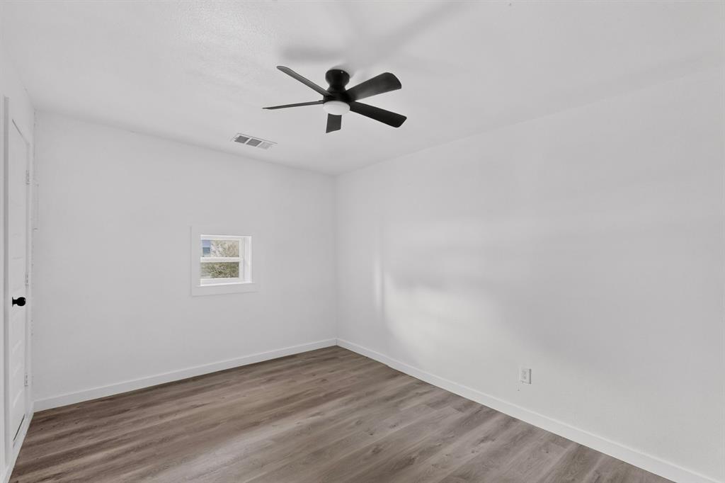 Interior space featuring wood-finish flooring, white walls, a multi-blade ceiling fan with integrated lighting, and a window with white trim