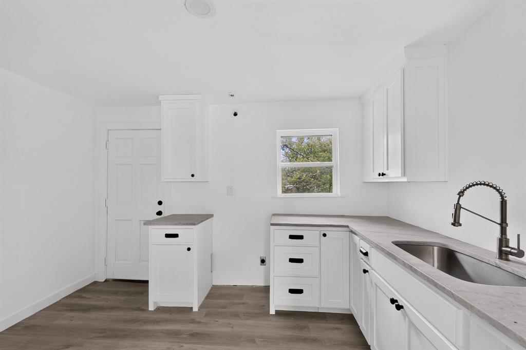 Kitchen featuring white shaker-style cabinetry, solid-surface countertops, wood-finish flooring, undermount stainless steel sink, and high-arc pull-down faucet