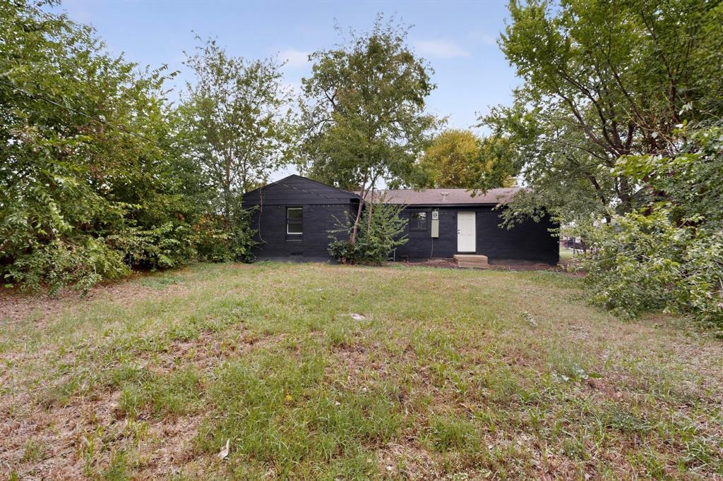 Exterior featuring a black brick facade, gable roofline, and mature trees situated on a grass-covered lot