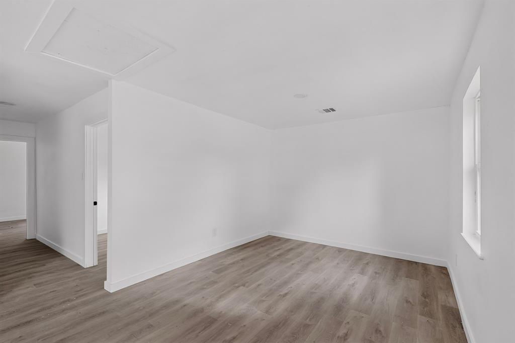 Neutral interior space featuring wood-finish flooring, crisp white walls, and a recessed ceiling access panel