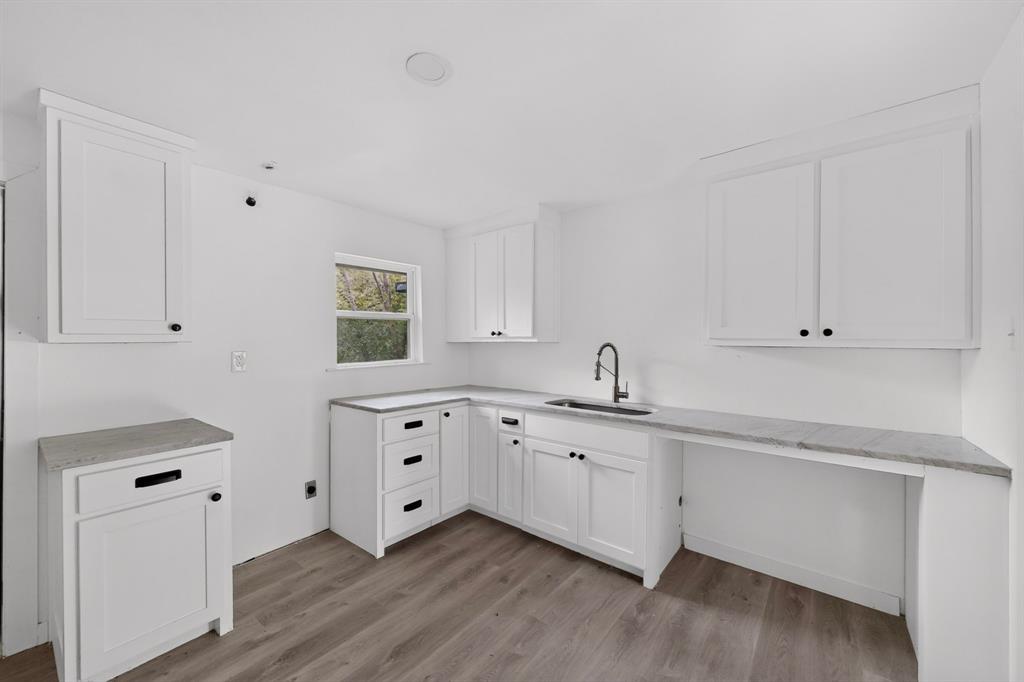 Kitchen featuring white cabinetry, stone-finish countertops, wood-finish flooring, undermount sink, and matte black hardware