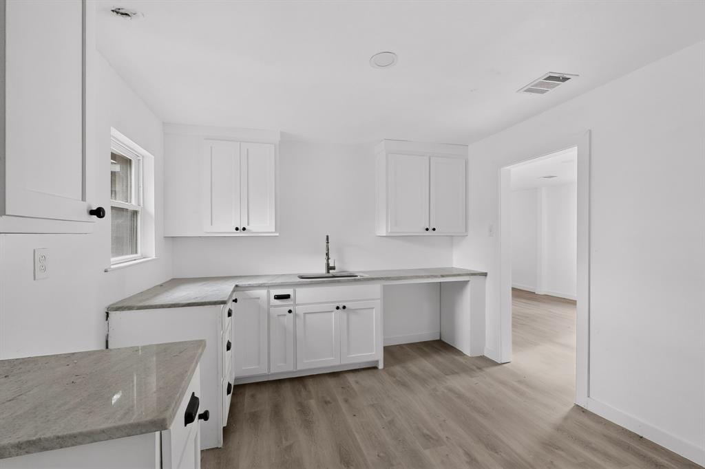 Kitchen featuring white shaker-style cabinetry, stone-finish countertops, undermount sink with a pull-down faucet, and wood-finish flooring