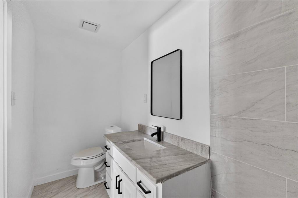 Bathroom featuring white cabinetry, stone-finish countertop, rectangular under-mount sink, matte black hardware, and large-format wall tile