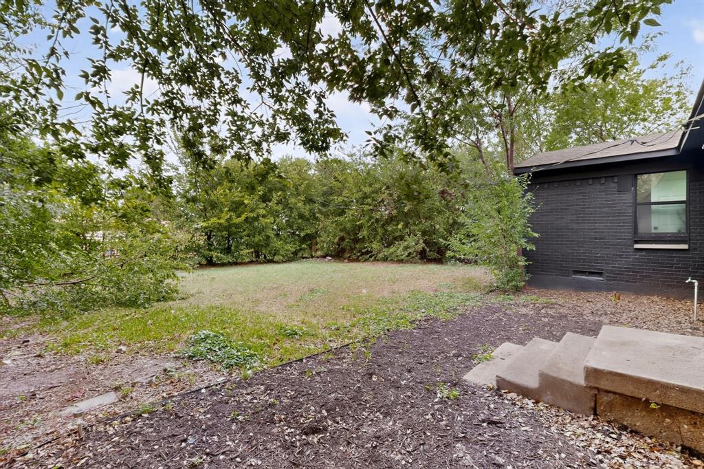 Backyard featuring a grass lawn, mature trees, concrete steps, and a dark-toned brick exterior