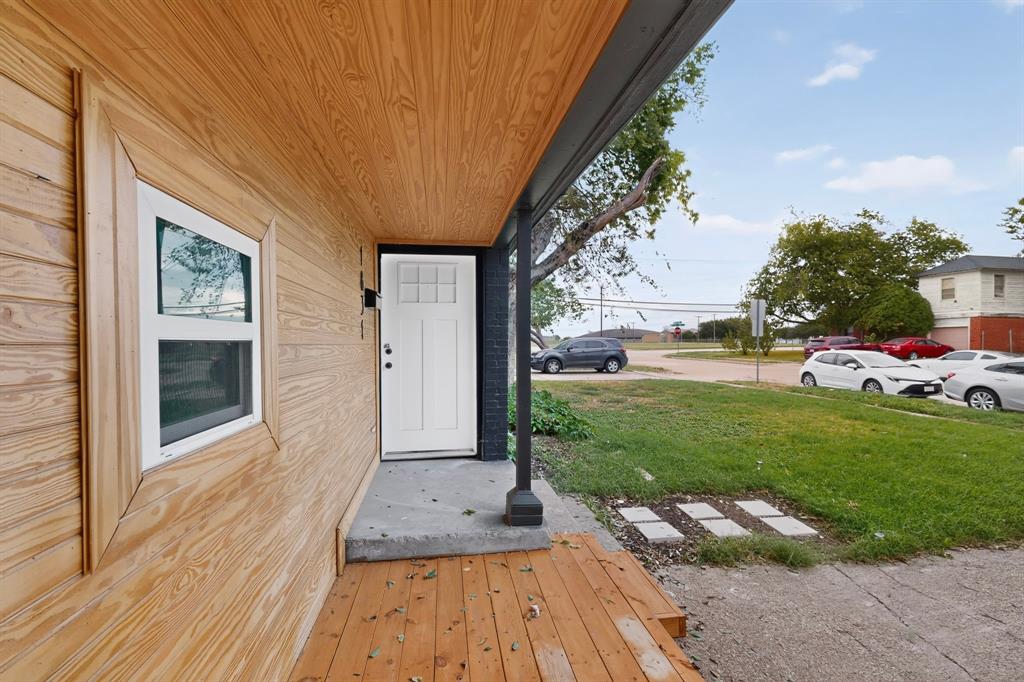 Exterior entryway featuring wood-finish siding, a covered wood-plank porch, a multi-pane front door, and dark-finished structural column