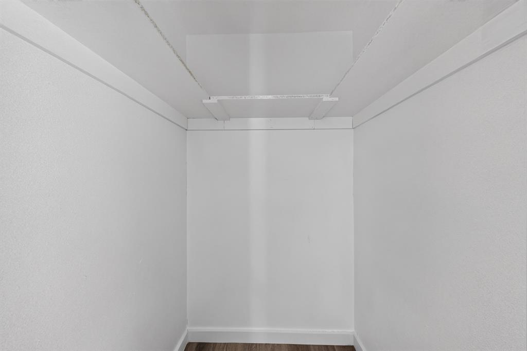 Storage area featuring white walls, wood-finish flooring, and a built-in overhead shelf