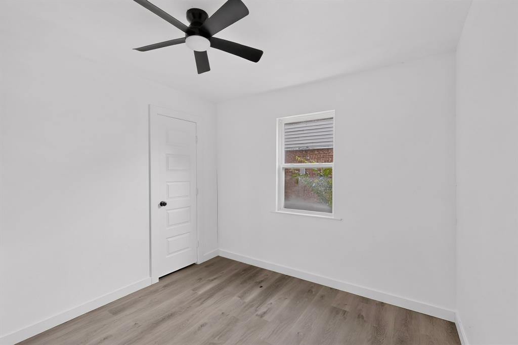 Interior space featuring wood-finish flooring, a five-panel interior door, a single-hung window, and a matte black ceiling fan