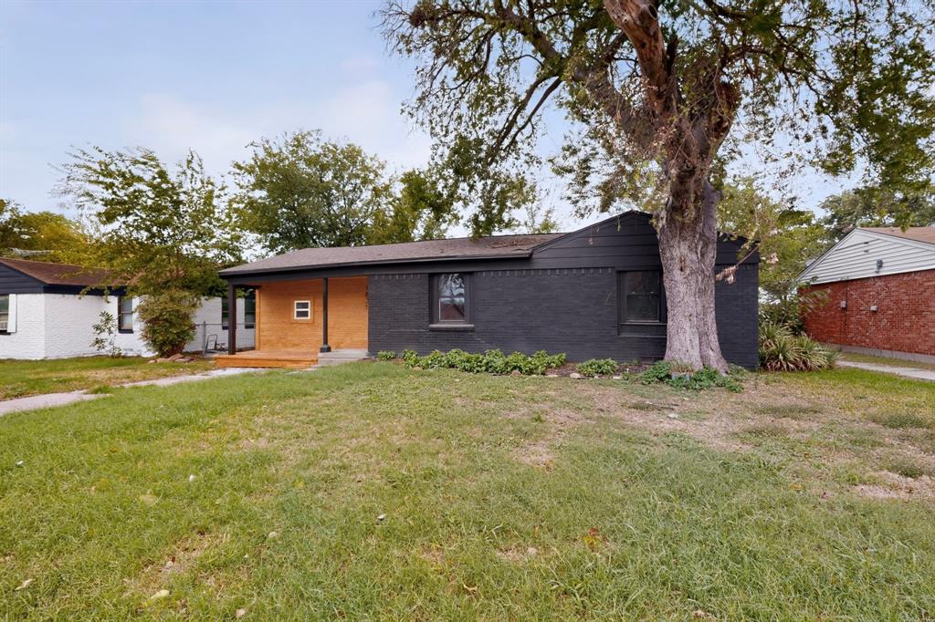 Exterior facade featuring painted brick masonry, natural wood-finish porch siding, dark-toned trim, and a mature tree