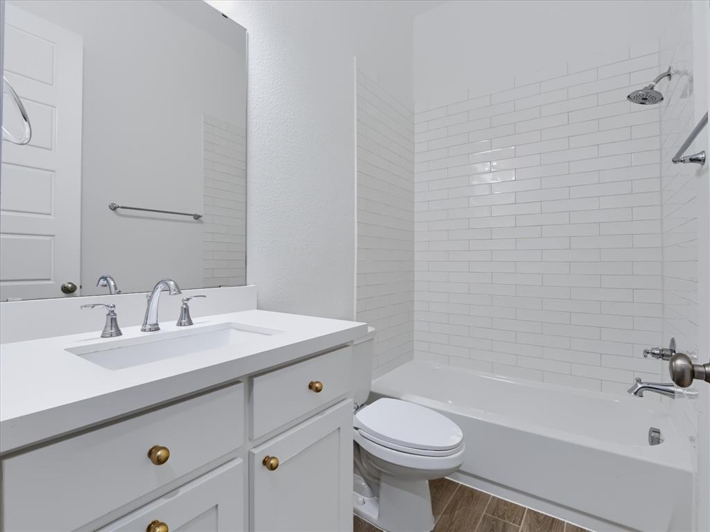 Bathroom featuring a white vanity with a composite countertop, undermount sink, brass hardware, subway tile tub surround, and wood-finish flooring