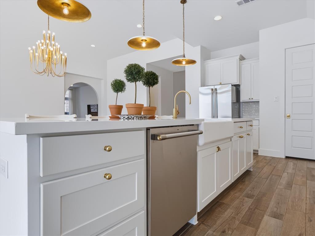Kitchen featuring a white island with cabinetry, farmhouse-style sink, brass-tone hardware, pendant lighting, and wood-finish flooring